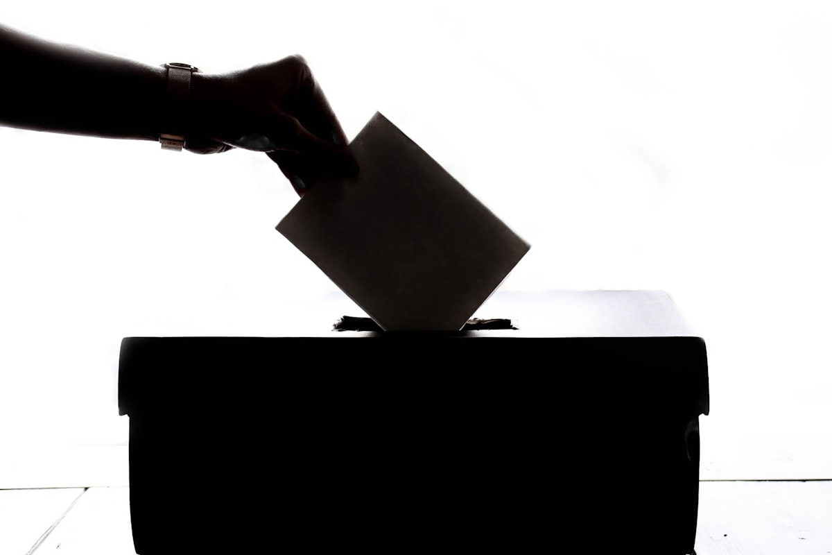 A hand casting a paper ballot into a ballot box